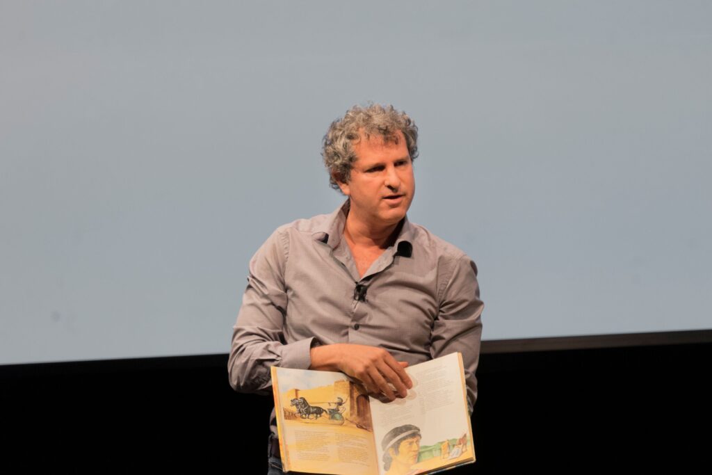 A man holds up an illustrated book, displaying two interior pages