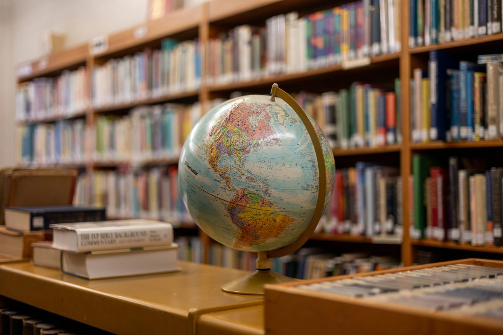 Book shelves in what appears to be a library, in the foreground a world globe is in focus.