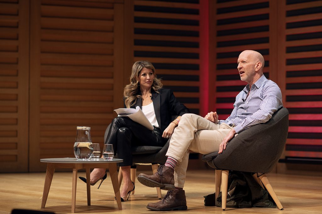 A man and a woman seated on a stage, engaged in conversation