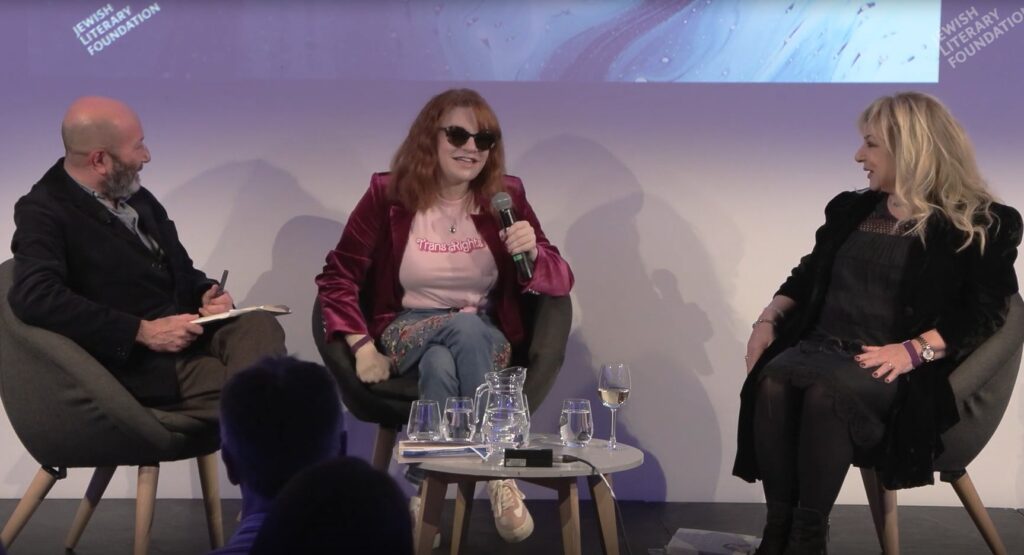 three people speaking, sitting on chairs, central woman with sunglasses