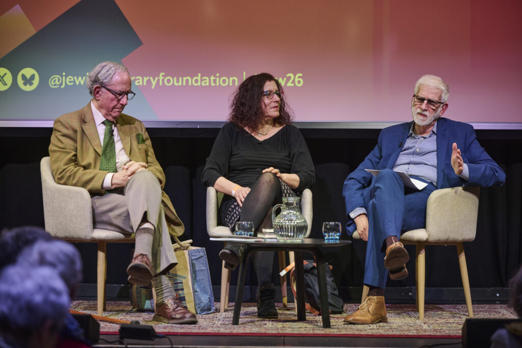 Two men and a woman sit on a stage, in conversation.