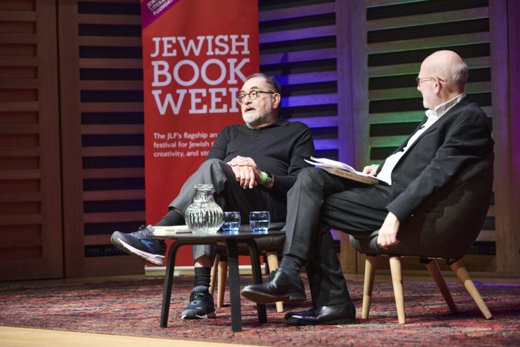 two men sitting in chairs on stage with pull up banner behind