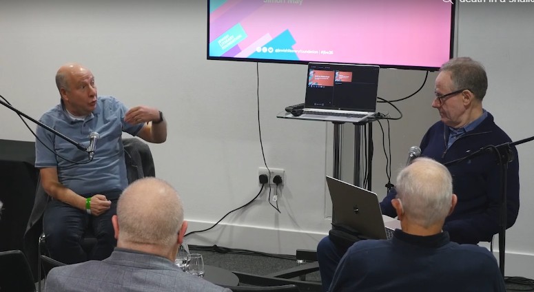 two men talking with screen behind