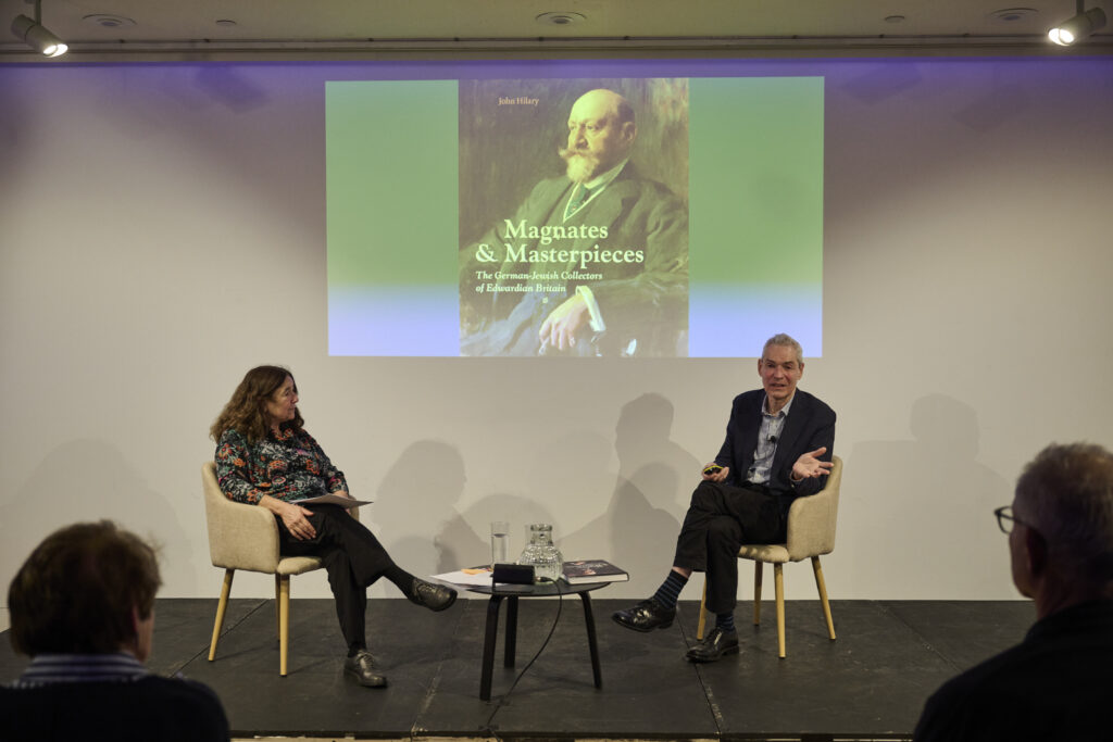 Two people sitting talking to each other with a projected screen behind, sitting on chairs