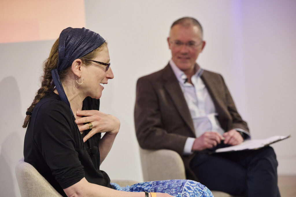 two people talking in a live event, a woman with her hand on her chest, talking to a man with a suit